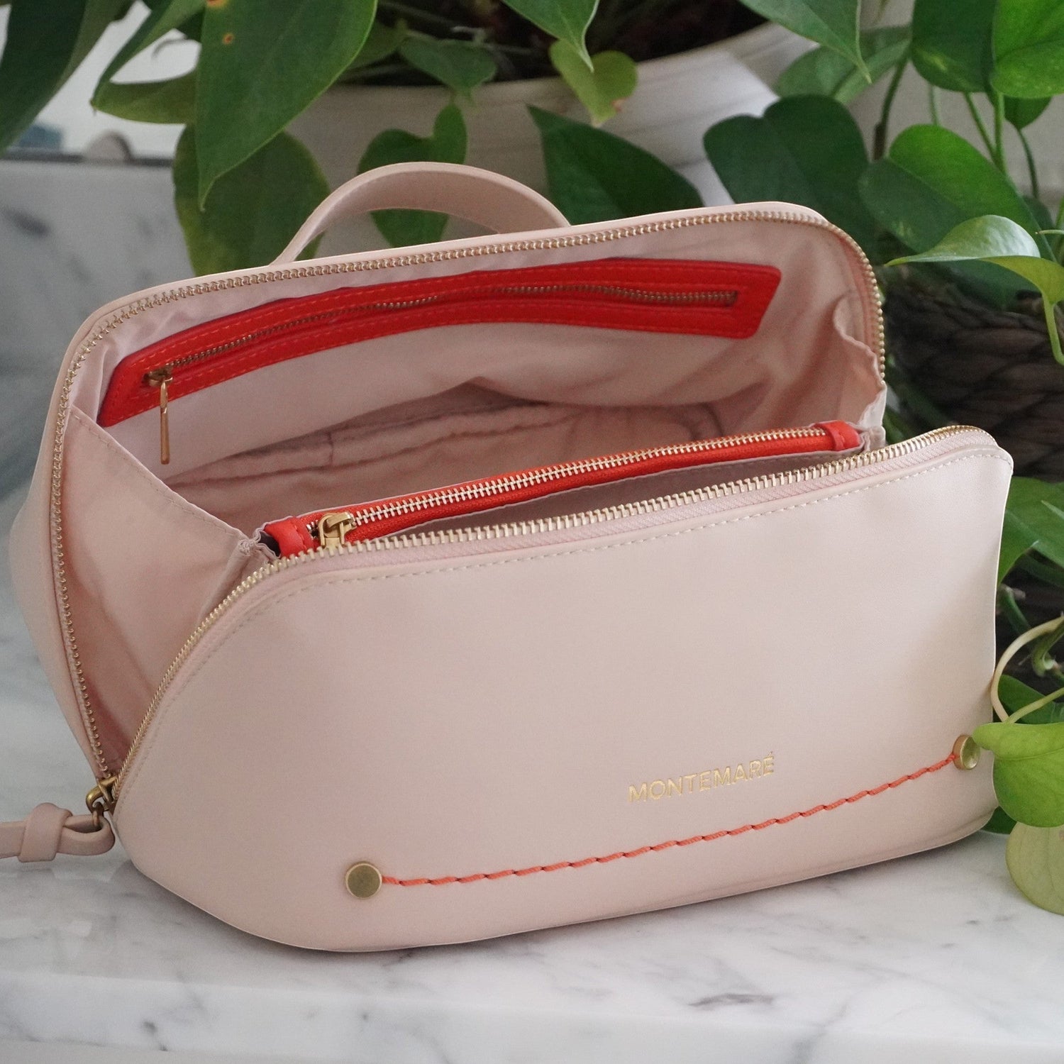 Montemaré Roma foldout toiletry case in blush pink vegan leather with orange accents and a wide zippered opening.