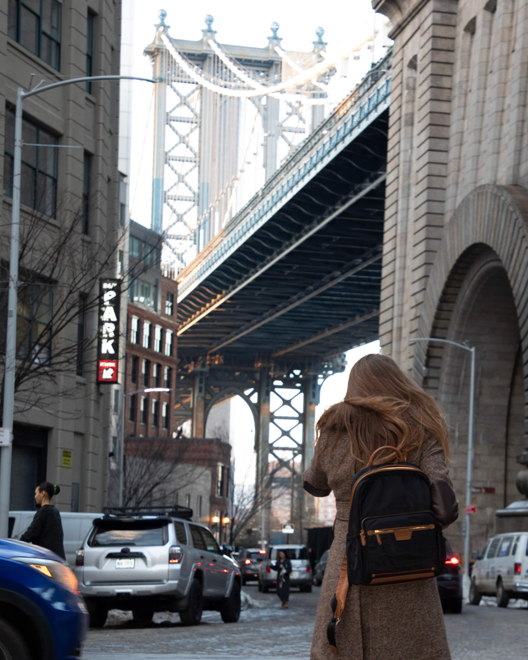 Person with a backpack walking on a city street with a bridge in the background