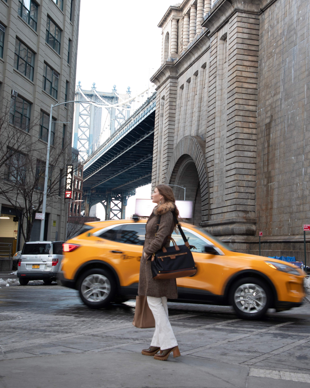 Woman with a black carry on bag walking on a city street with a yellow taxi in the background