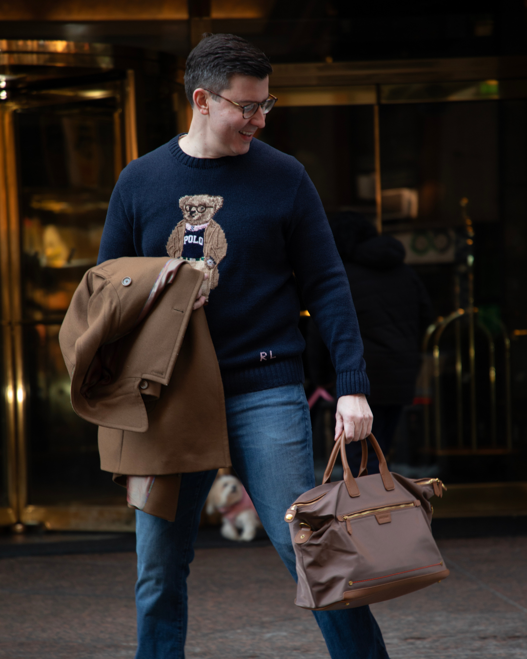 Man holding a brown jacket and bag outside a hotel lobby