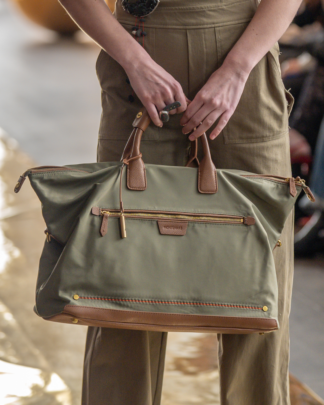 Person holding a green carry on bag with brown leather handles and trim.