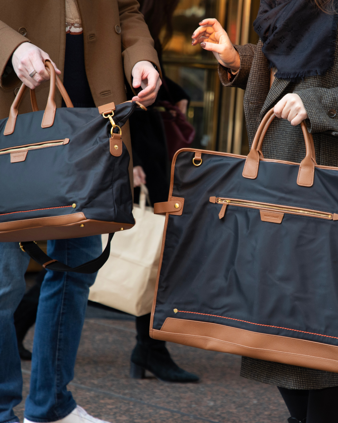 Black garment bags held by two people outside building
