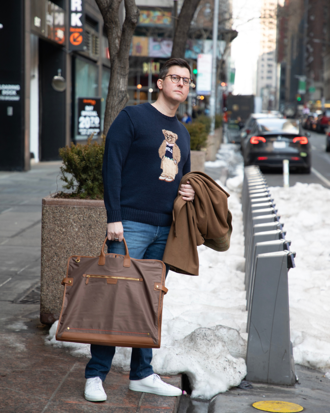 Man holding a brown garment bag on a city street with snow.
