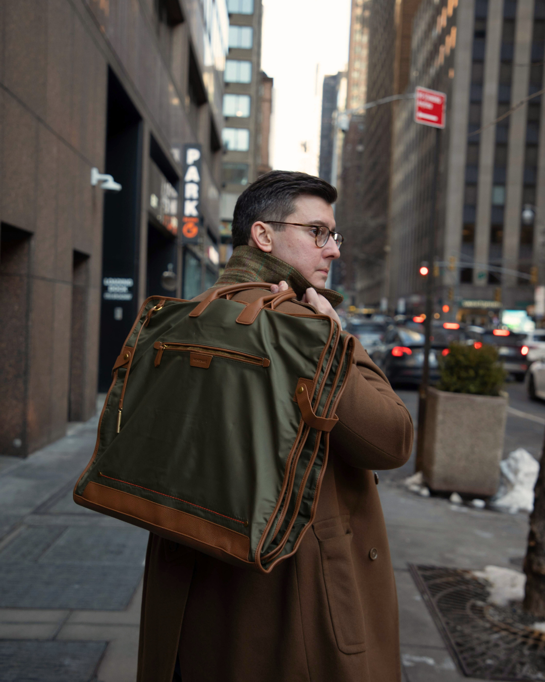 Man holding a green and brown garment bag on a city street