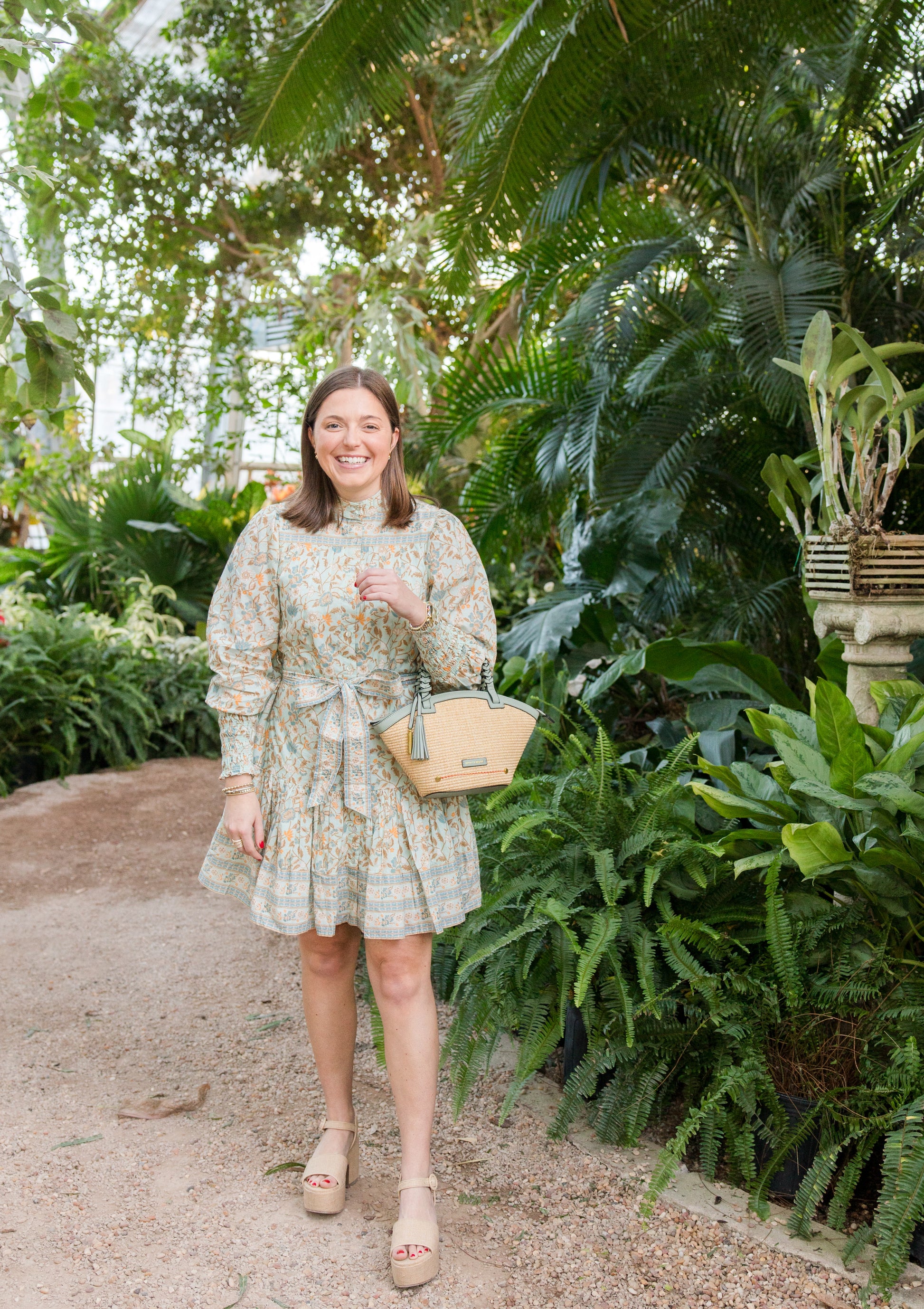 Woman in a floral dress with a beach bag standing in a lush garden