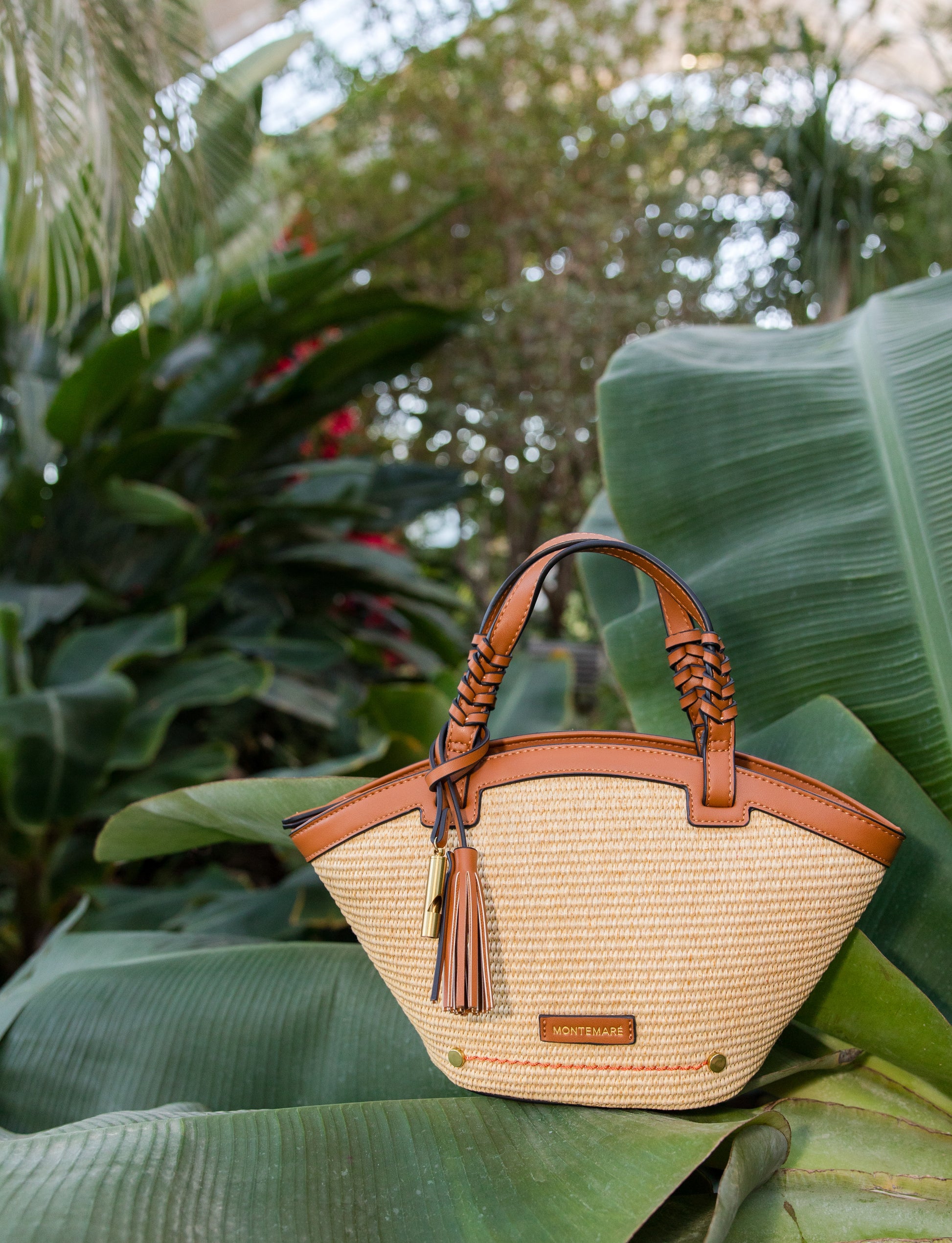 Woven handbag with cognac leather accents on a leafy green background