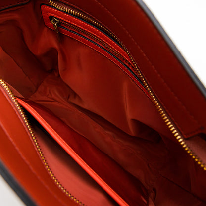 Close-up of a leather bag with gold zipper and orange interior accents