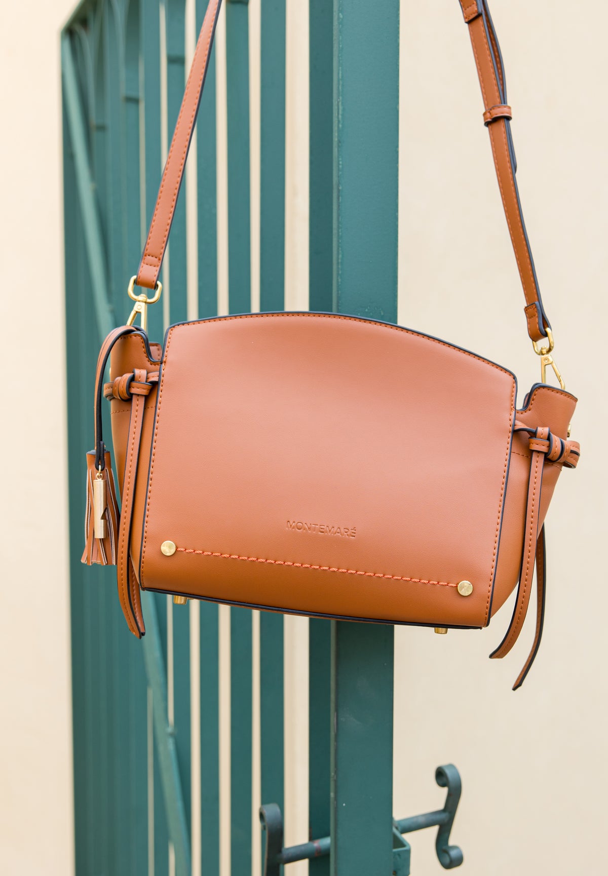 Brown leather handbag with a strap against a green metal gate background