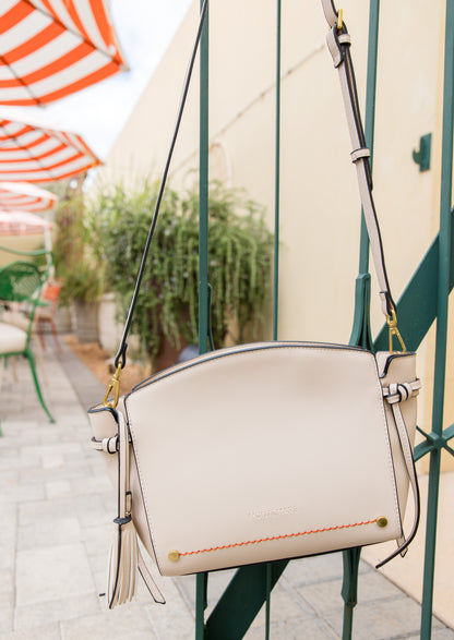 Beige handbag with orange accents hanging on a green metal fence with striped umbrellas in the background.