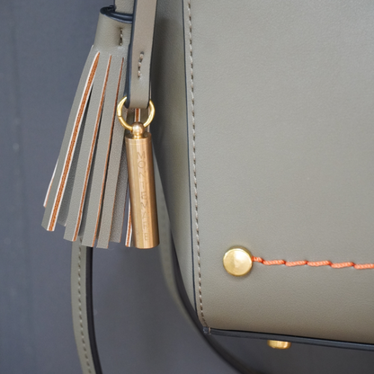Close up shot of Montemare Roma Crossbody in olive colorway with orange thread accent, whistle tassel on a gray background