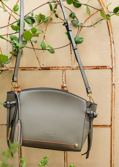 Olive green handbag with gold accents on a beige wall with greenery