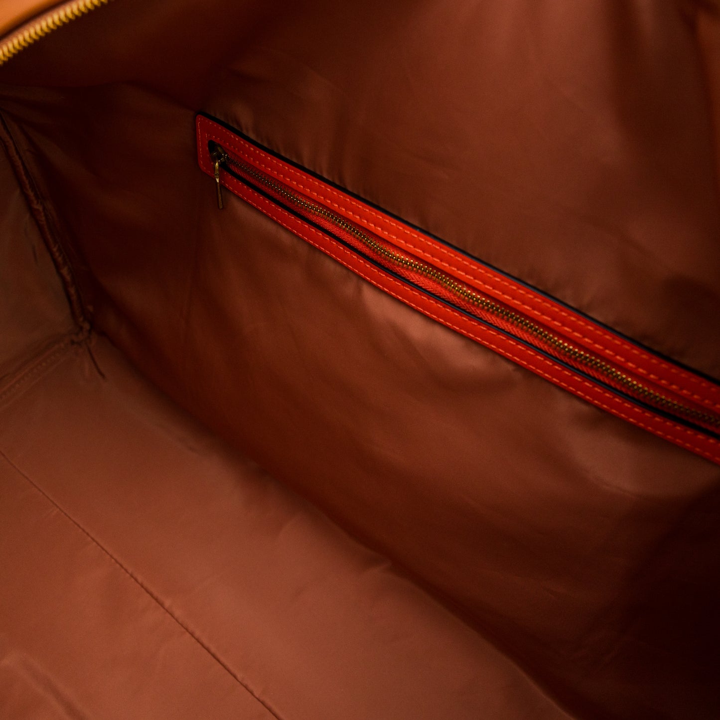 Close-up of a brown leather bag with an orange zipper.