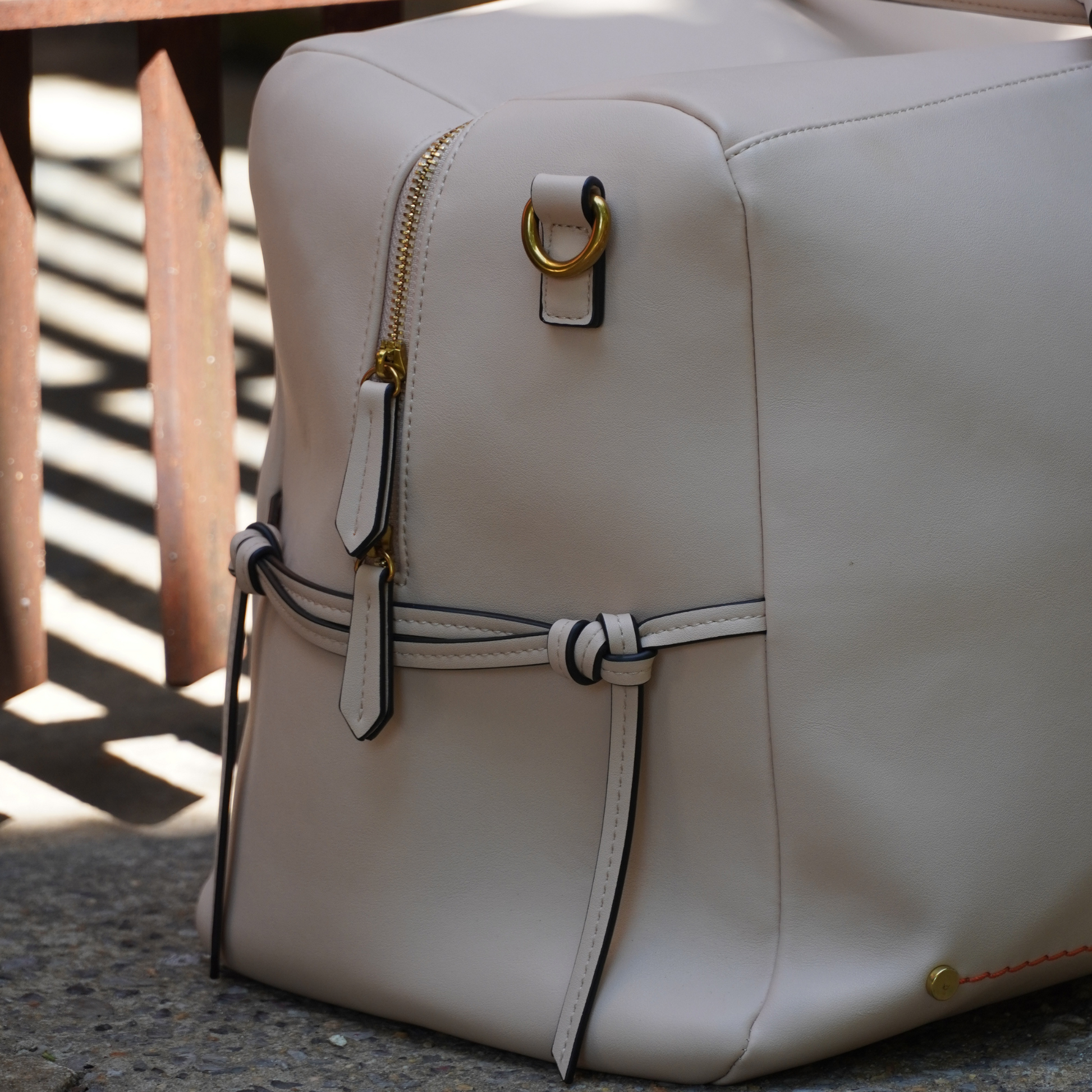 A detailed shot of Montemare Roma Duffel in ivory colorway with gold zippers and sling hook sitting on a floor
