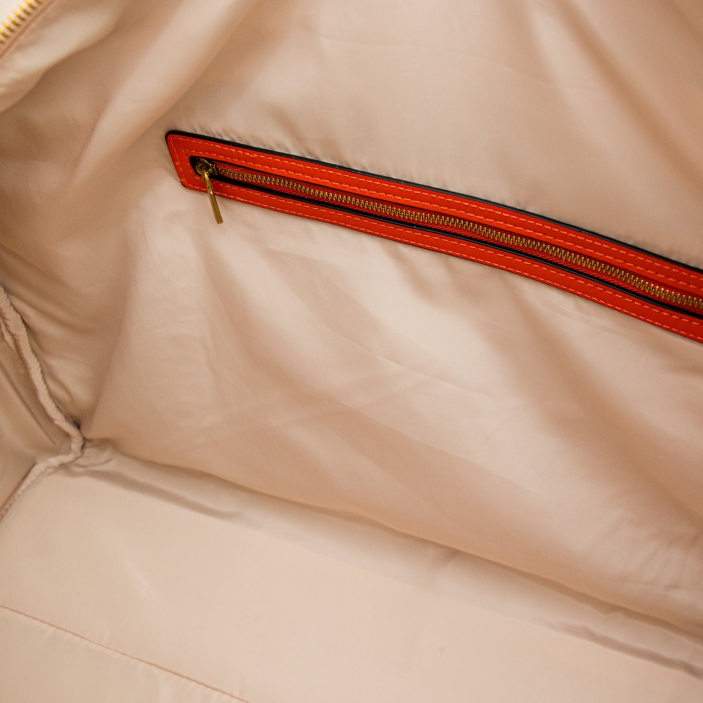 Close-up of a beige duffel bag with an orange zipper