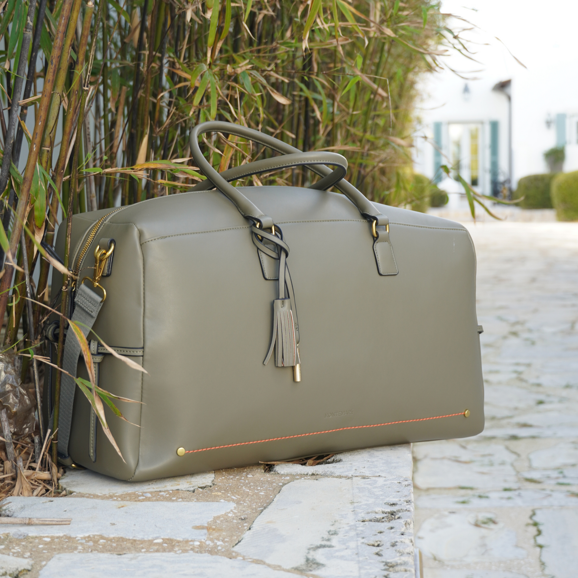 Olive green Montemare Duffel Bag sitting on a cobblestone floor with bamboo on the background