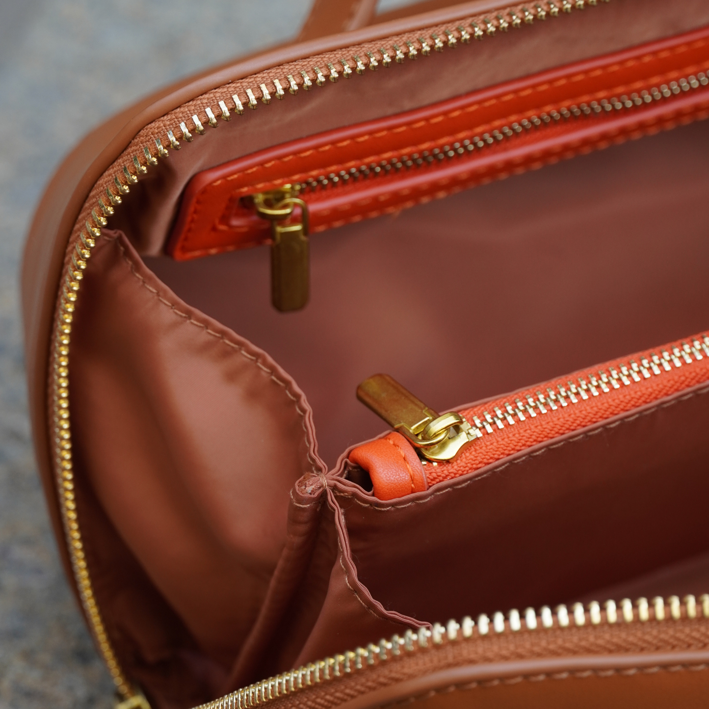 A close up shot of a cognac colored toiletry case with orange interior accents and gold zippers