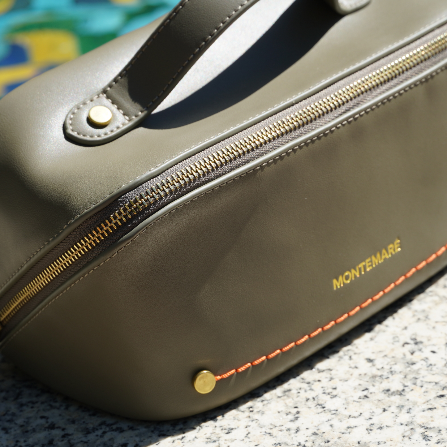An olive green toiletry case with Montemare branding and orange thread on top of a marble surface