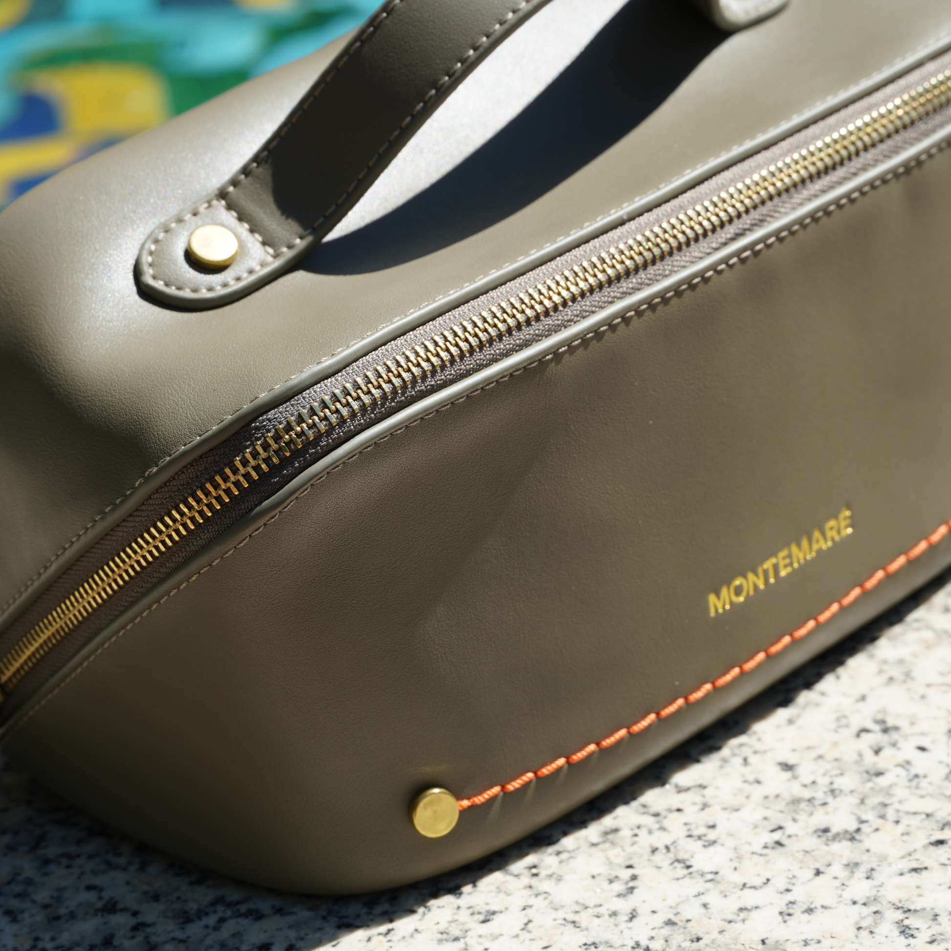 An olive green toiletry case with Montemare branding and orange thread on top of a marble surface