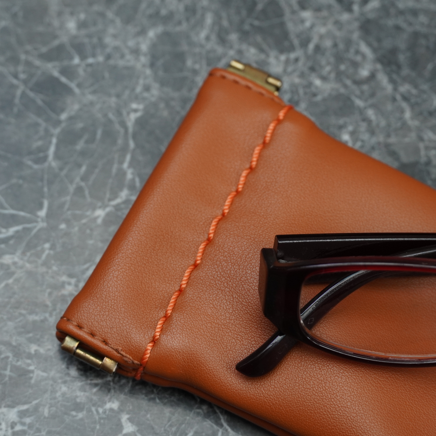 Montemare Roma glasses case in cognac colorway with eyeglasses on top sitting in a marble surface