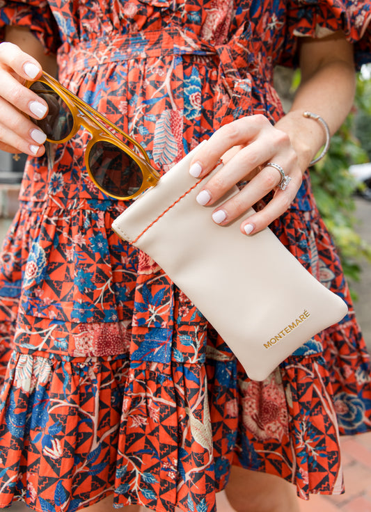 Person holding sunglasses and a beige pouch with 'Montemare' branding, wearing a colorful dress.