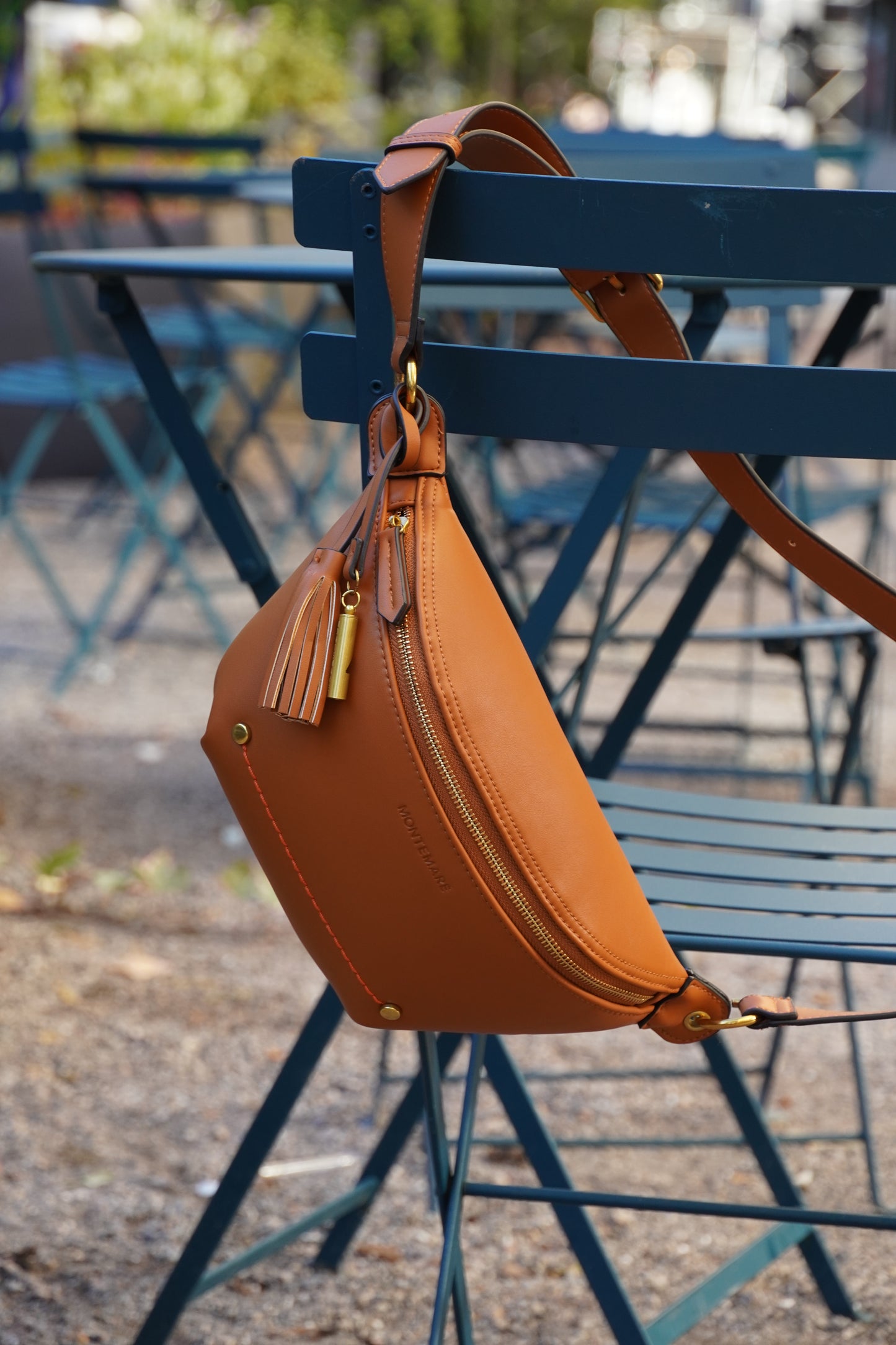 Brown leather waist bag hanging on a blue metal structure with a blurred background