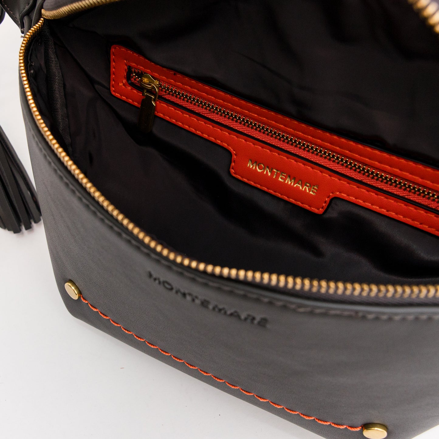 Close-up of a soft black leather bag with orange interior trim with 'Montemaré' branding and brass-finished zipper.