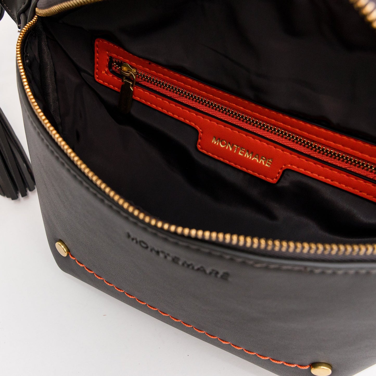 Close-up of a soft black leather bag with orange interior trim with 'Montemaré' branding and brass-finished zipper.