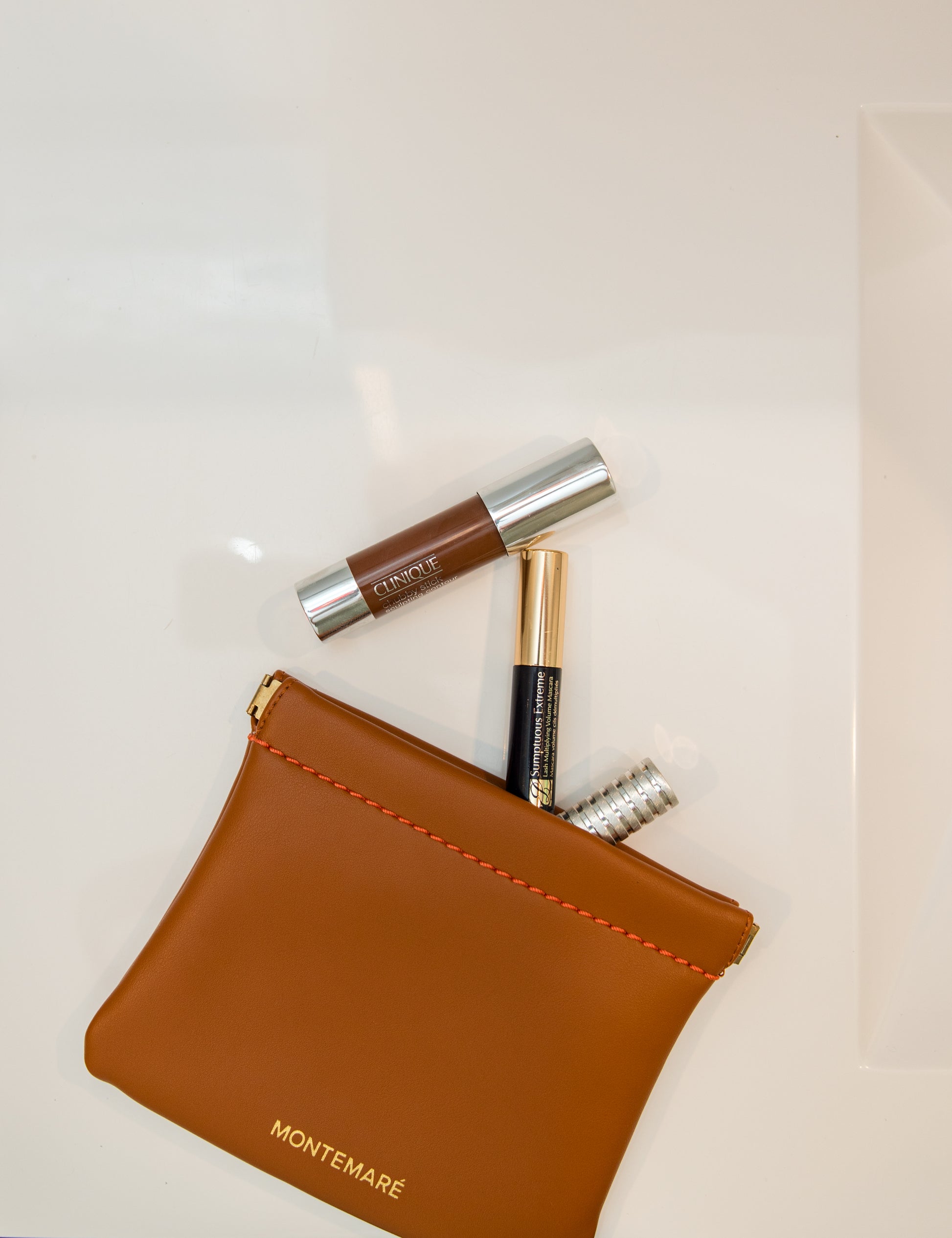 Brown leather pouch with cosmetic items on a light background