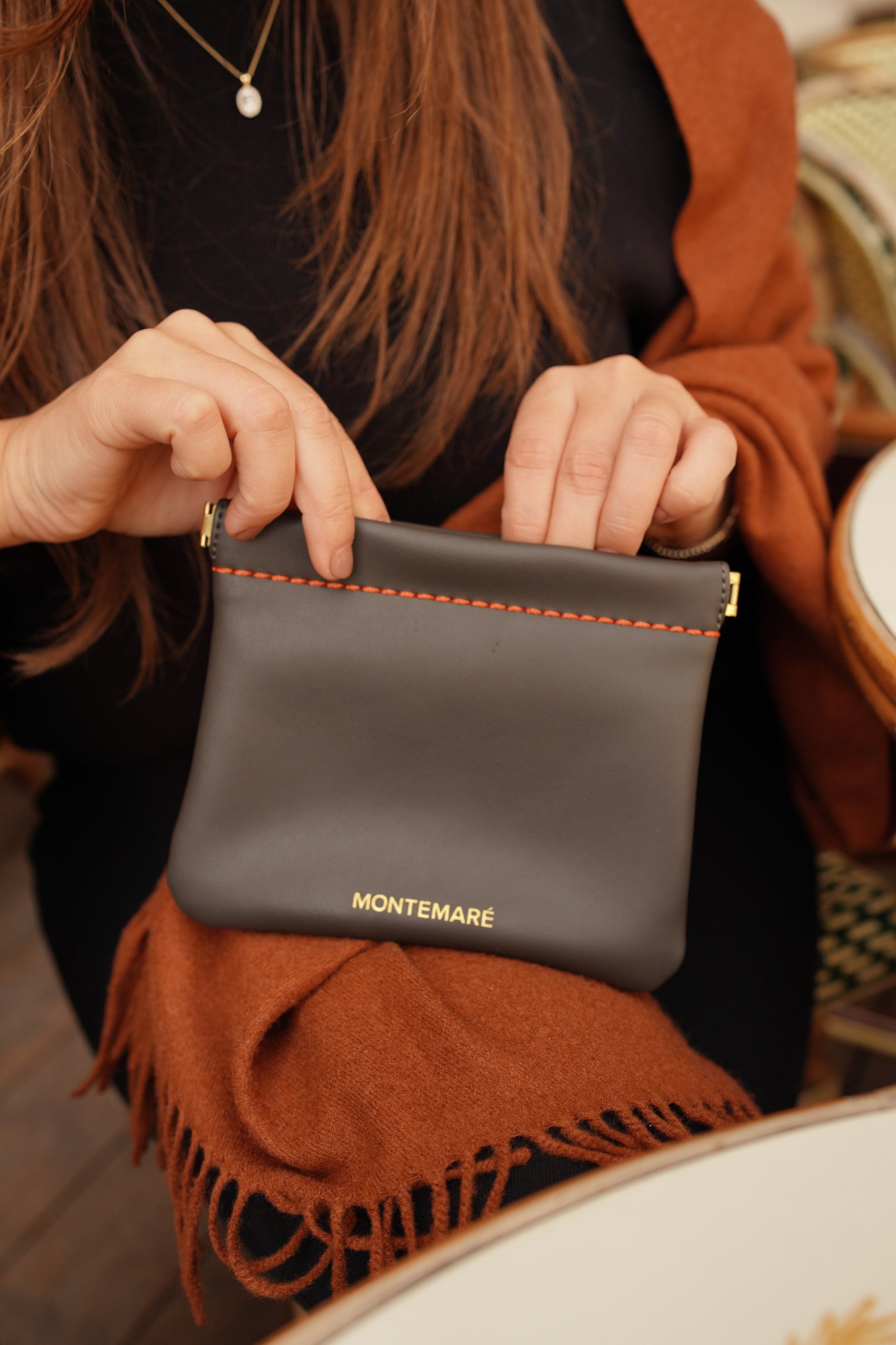 Person holding a dark brown leather pouch with 'MONTEMARE' branding.