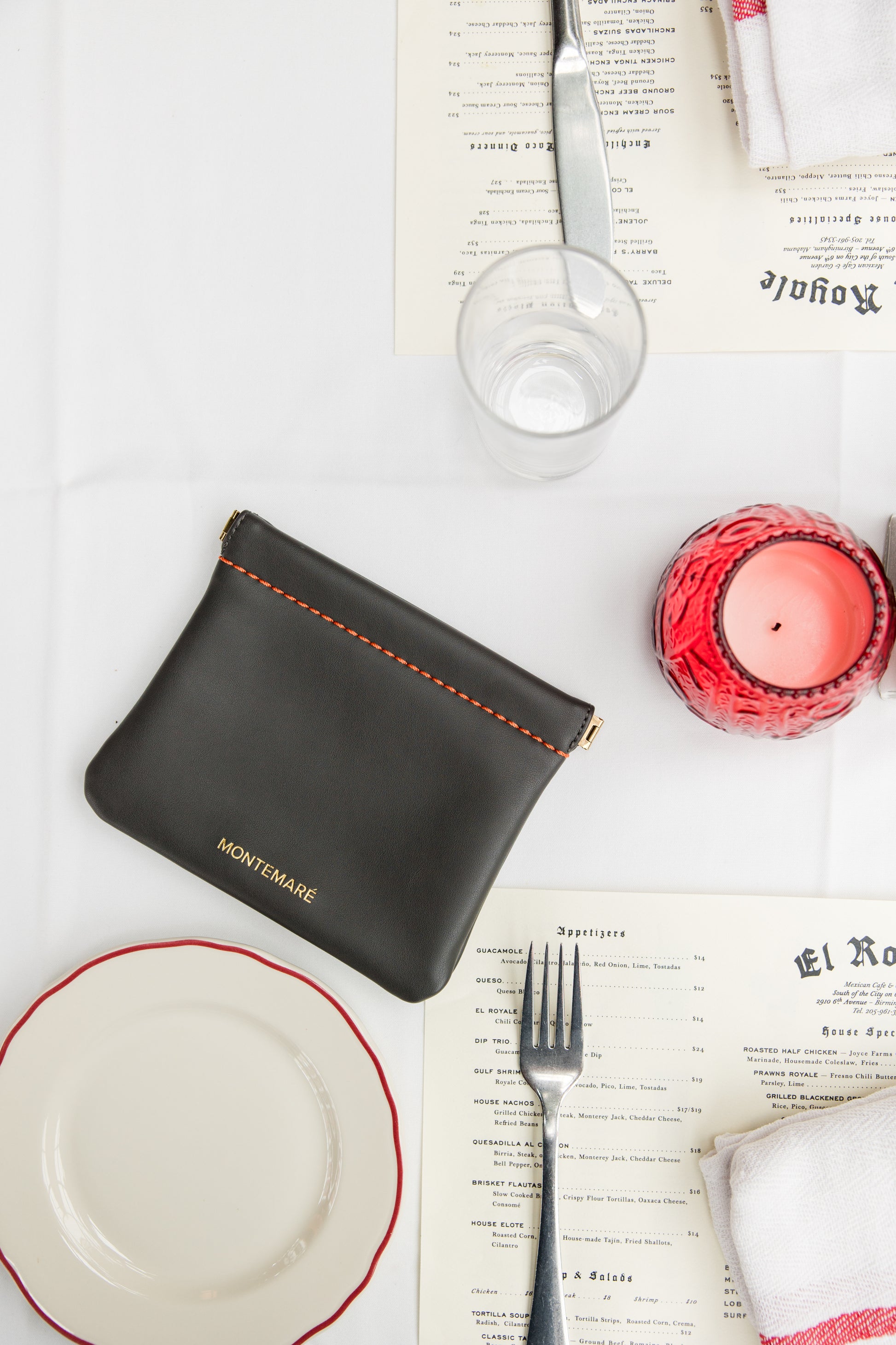 Black leather pouch on a table setting with plates, cutlery, and a candle.