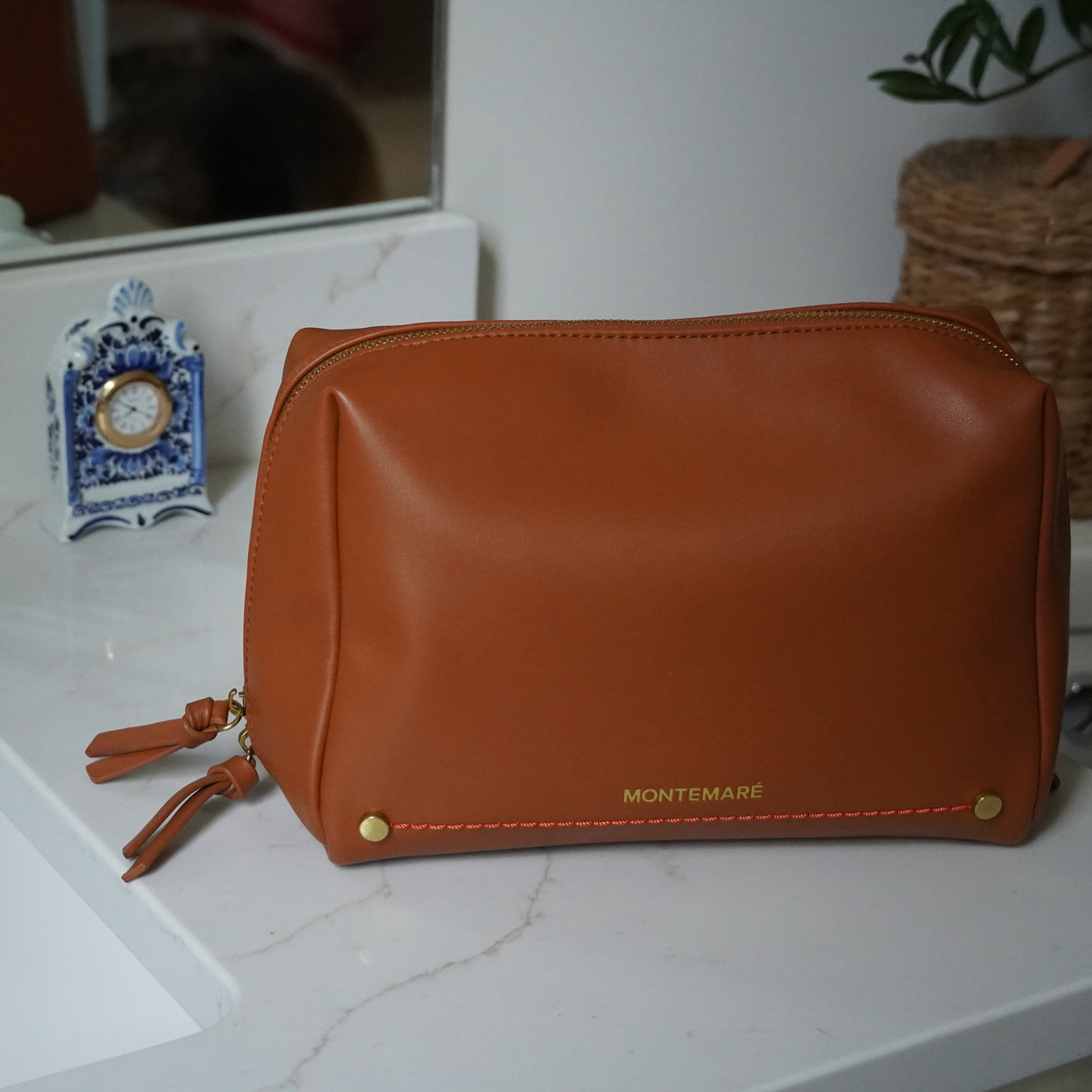 A brown standing toiletry case with Montemare branding and orange thread accent sitting on top of a marble surface