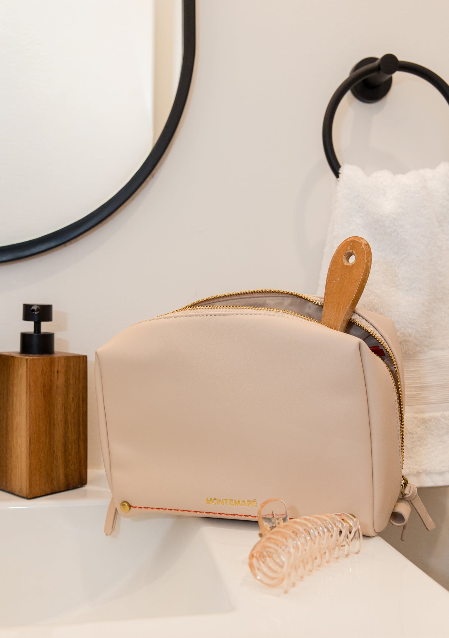 Ivory cosmetic bag with wooden hairbrush on a white surface with mirrors in the background