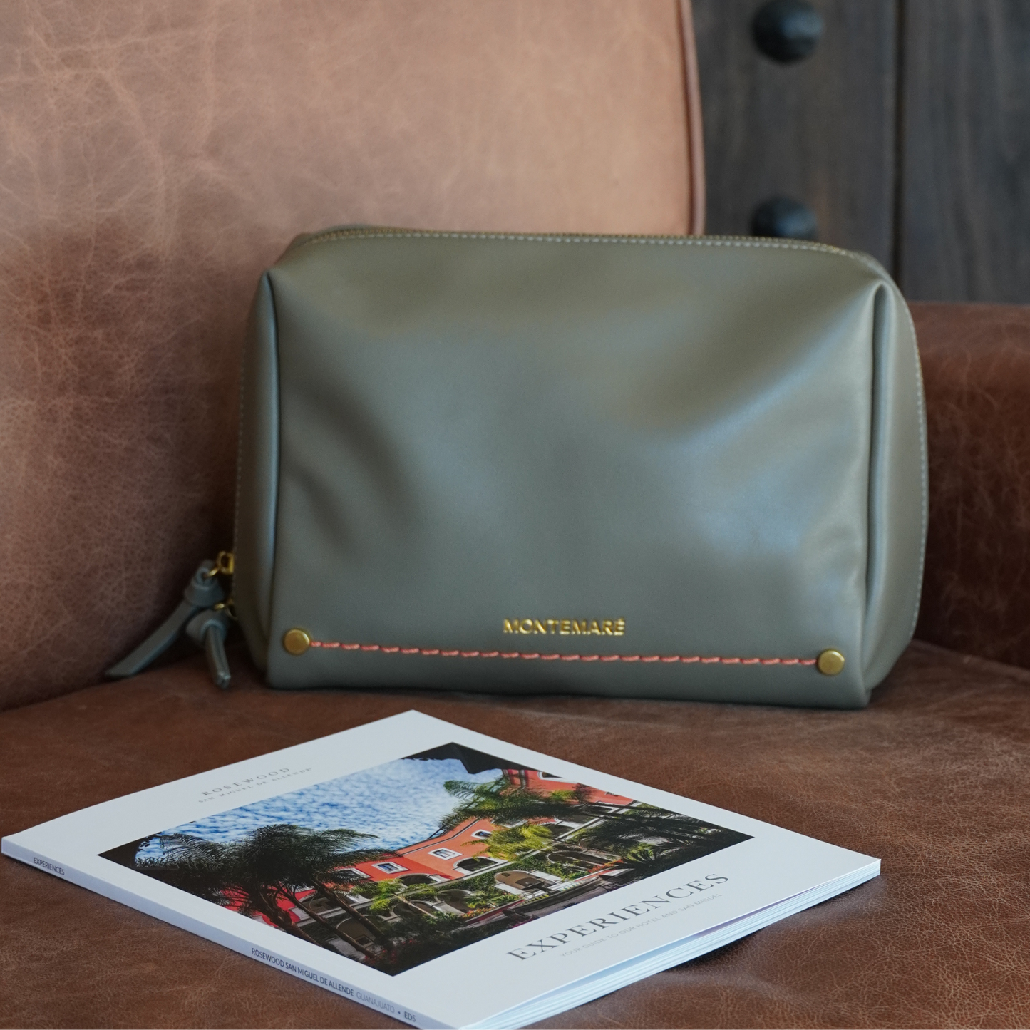Green leather pouch with 'Montemare' branding on a brown leather surface next to a book.