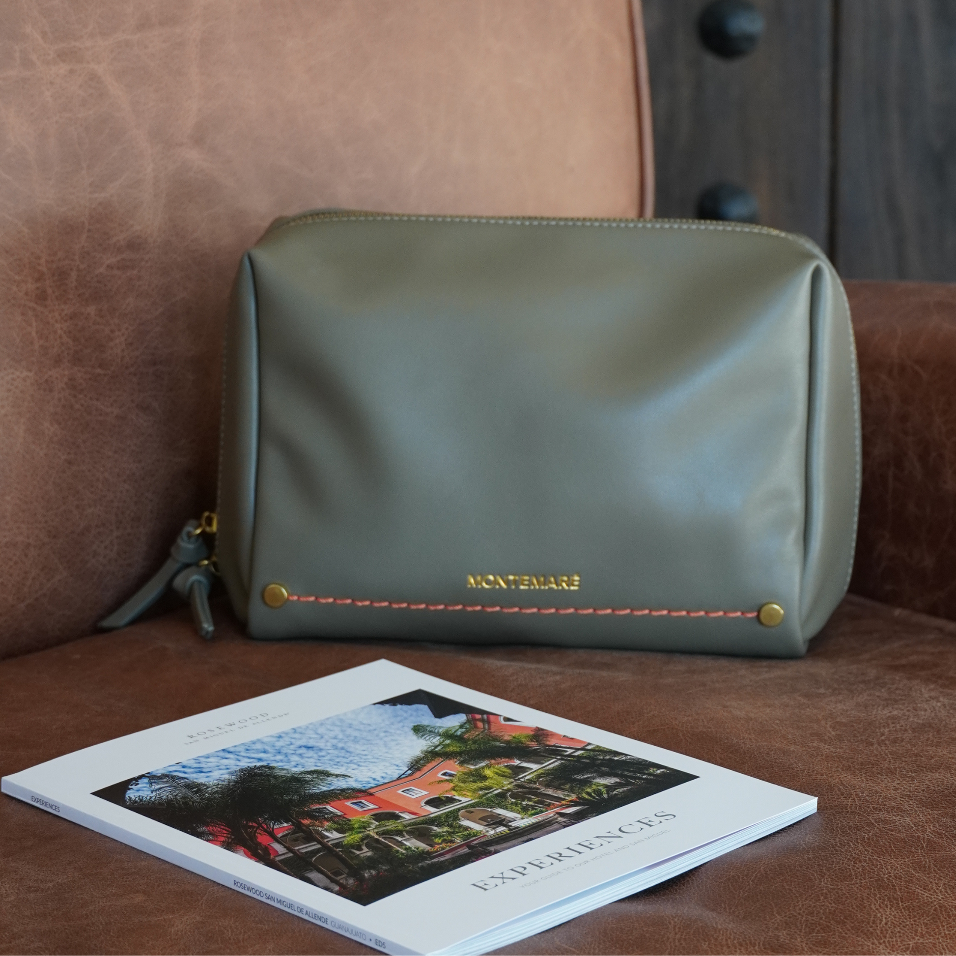 Green leather pouch with 'Montemare' branding on a brown leather surface next to a book.