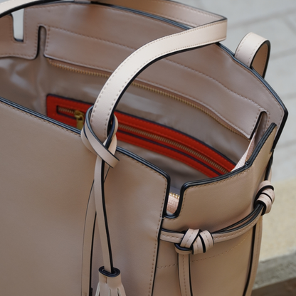 Close up shot of Montemare Roma Tote in ivory colorway with orange interior accent, tassles, gold zippers