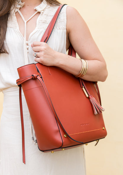 Person holding a terracotta leather bag against a beige background
