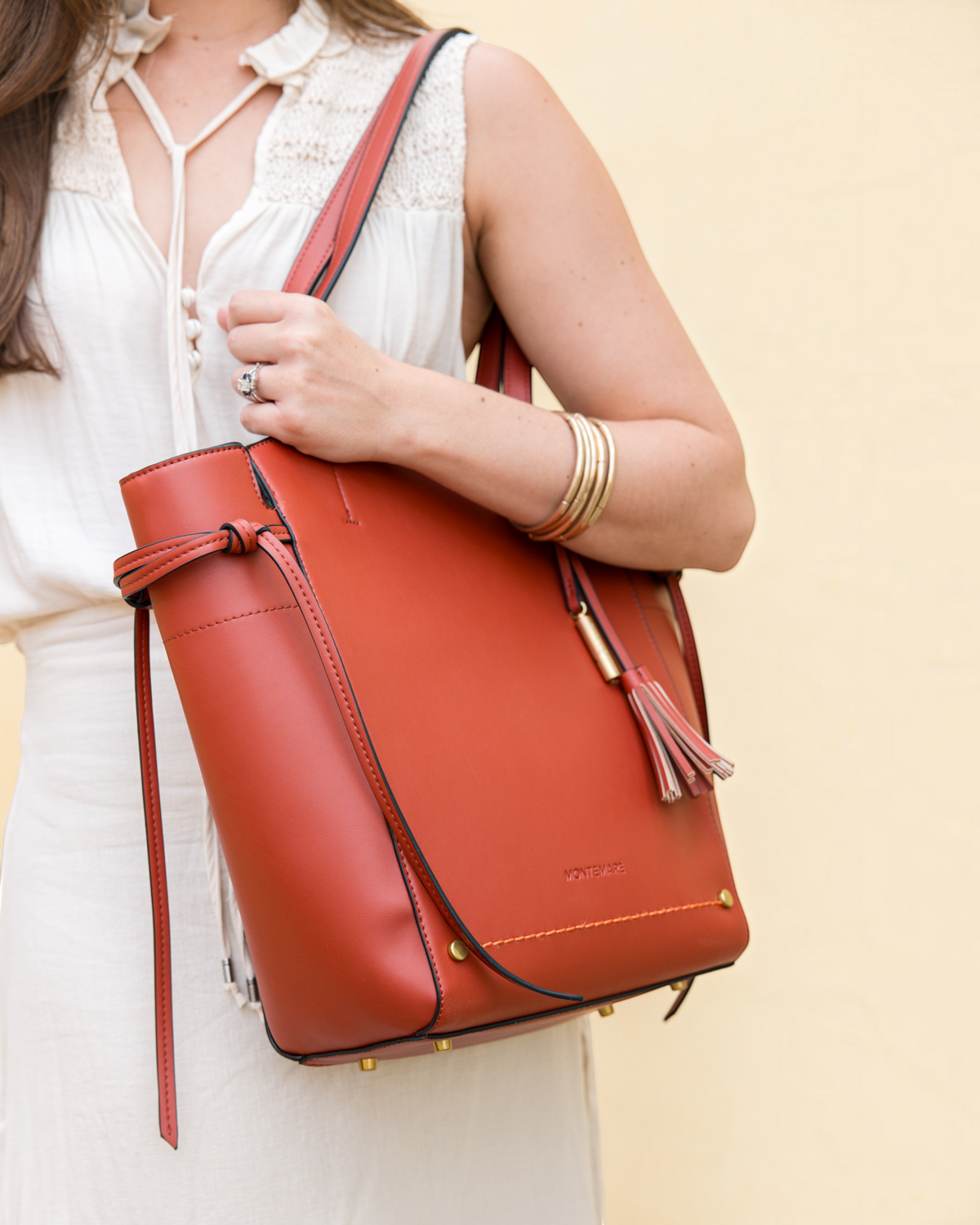 Person holding a terracotta leather bag against a beige background