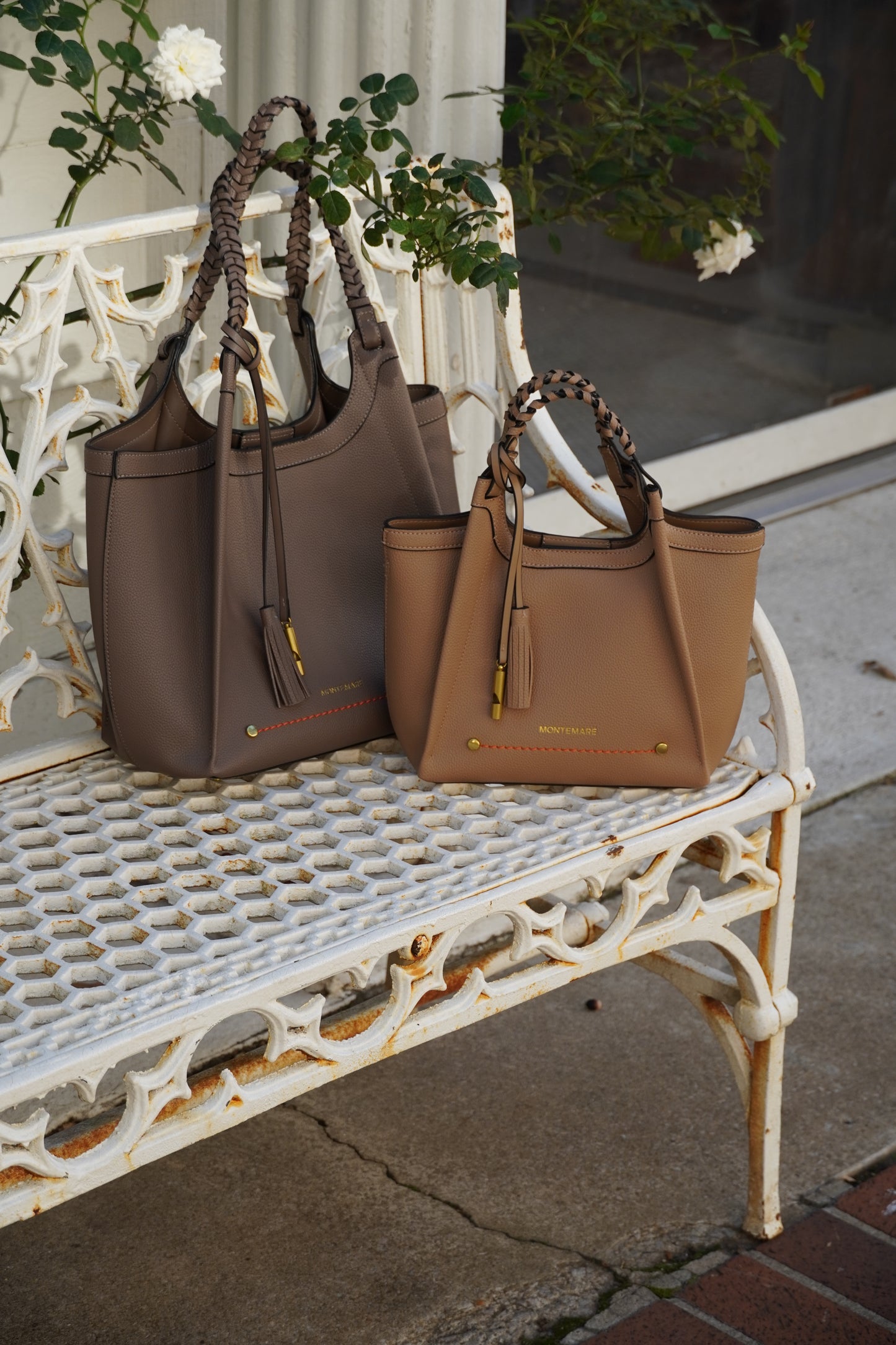 Two elegant handbags on a decorative white metal bench with flowers in the background.