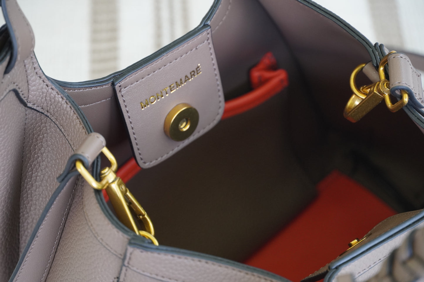 Close-up of a brown handbag with gold hardware and orange interior.