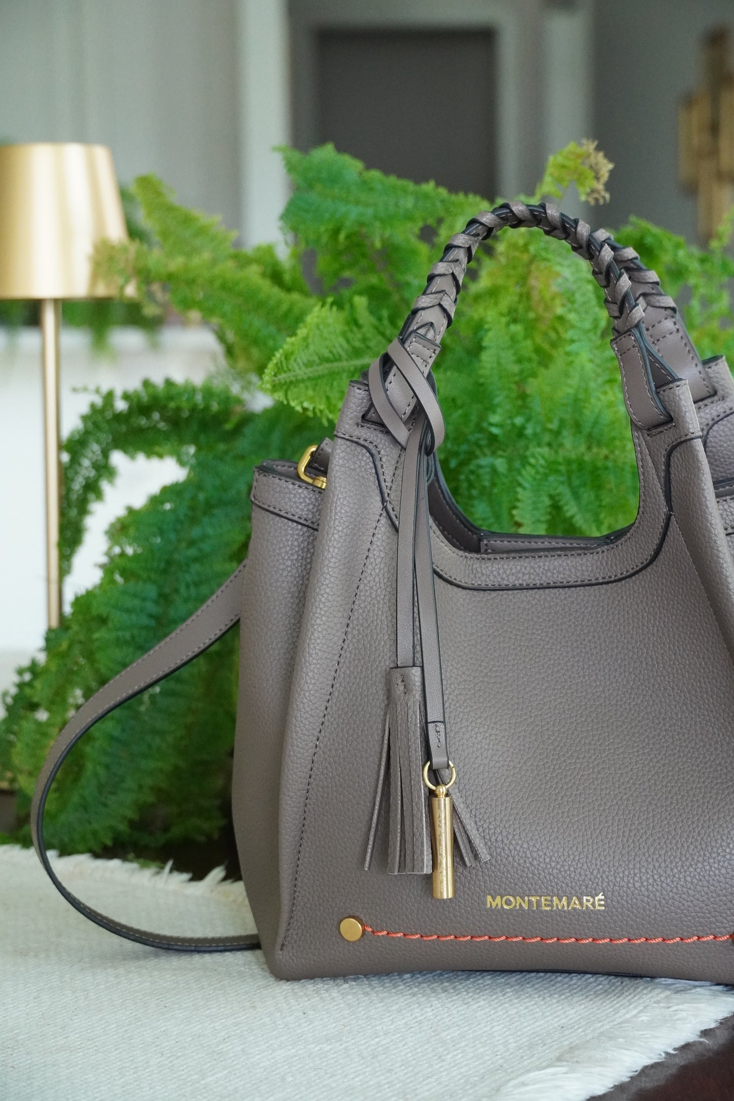 Brown handbag with a tassel detail on a decorative stand with greenery