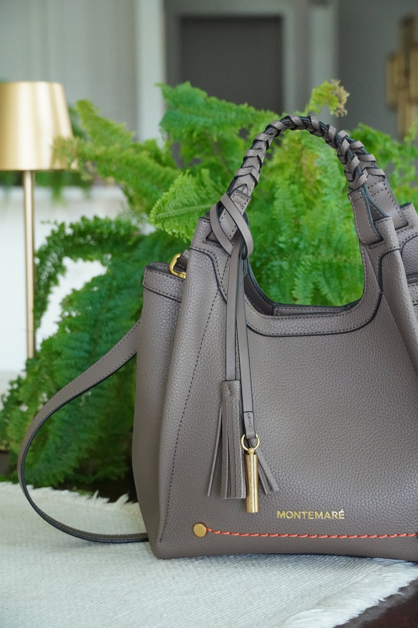 Brown handbag with a tassel detail on a decorative stand with greenery