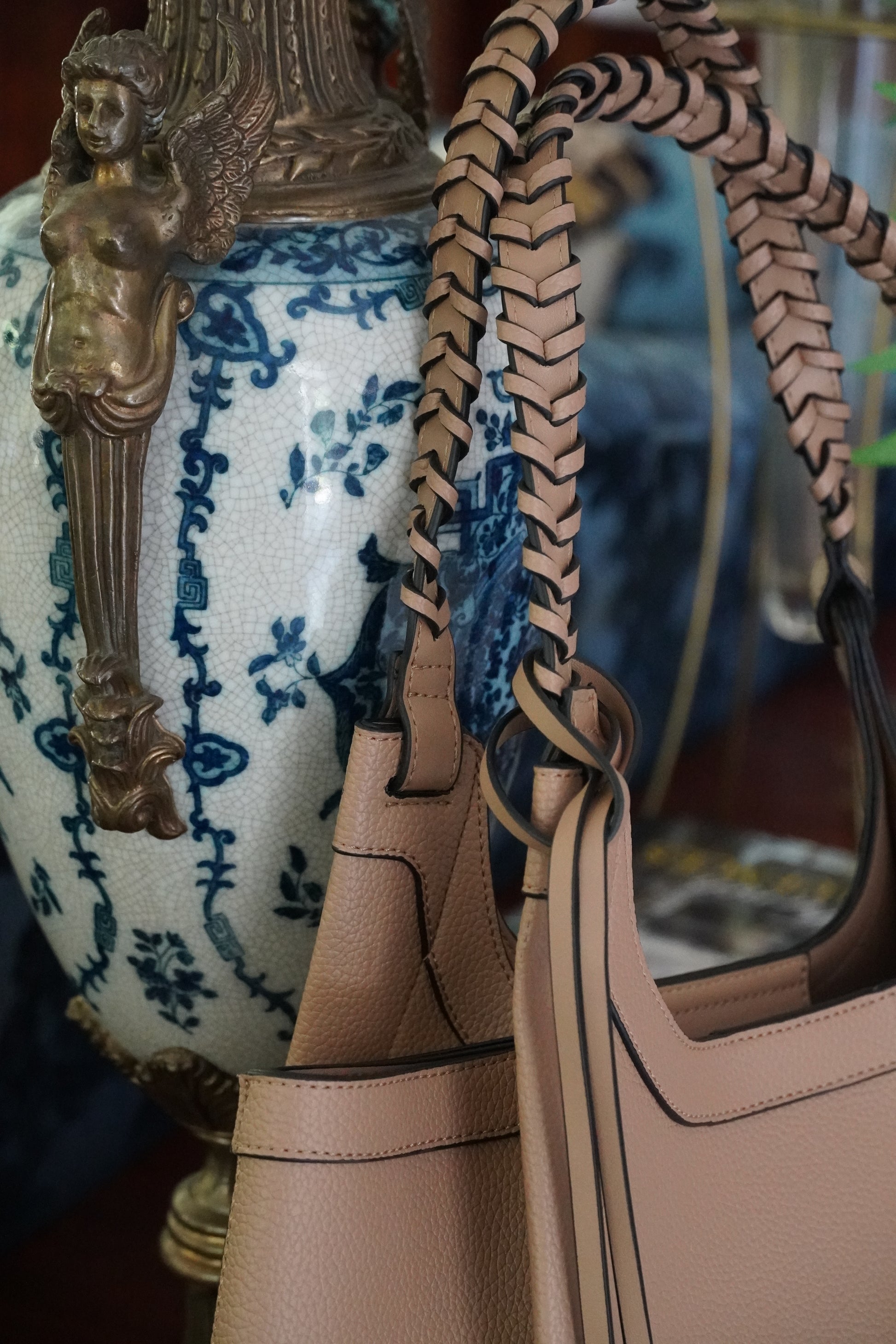 Close-up of a beige handbag with a woven strap on a decorative surface.