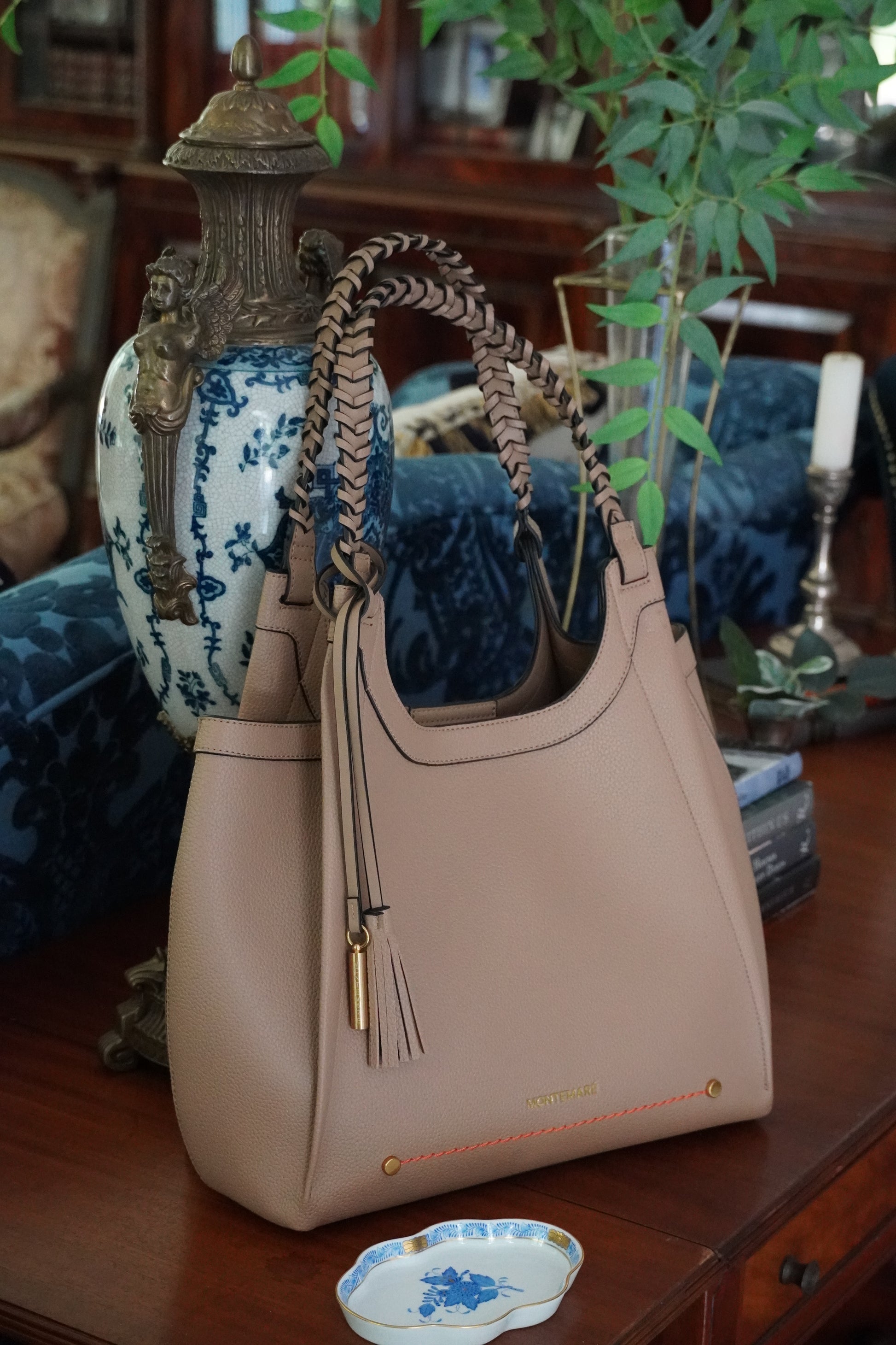 Beige handbag with tassels on a decorative surface with plants and books in the background