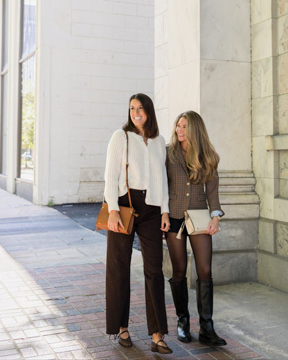 Two women with crossbody bags standing on a sidewalk next to a building