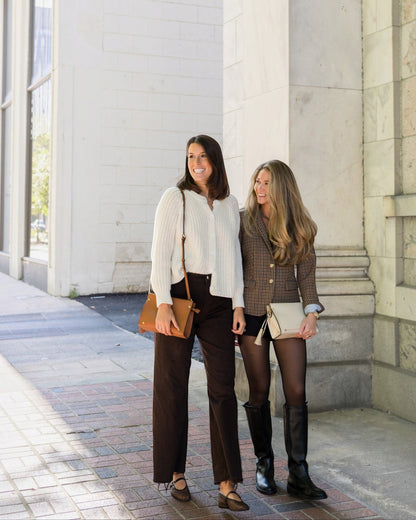Two women with crossbody bags standing on a sidewalk next to a building