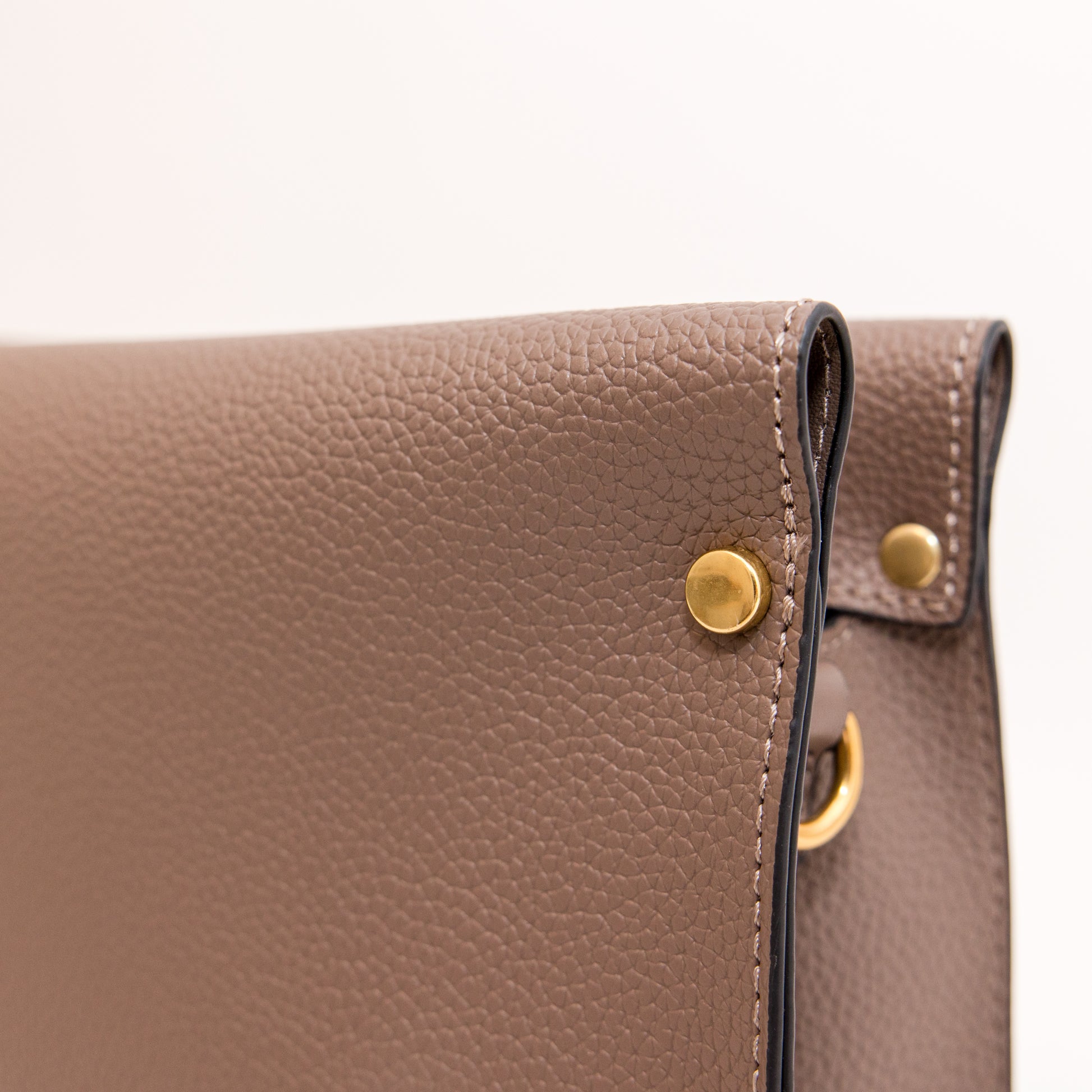 Close-up of a brown leather handbag with gold hardware on a white background