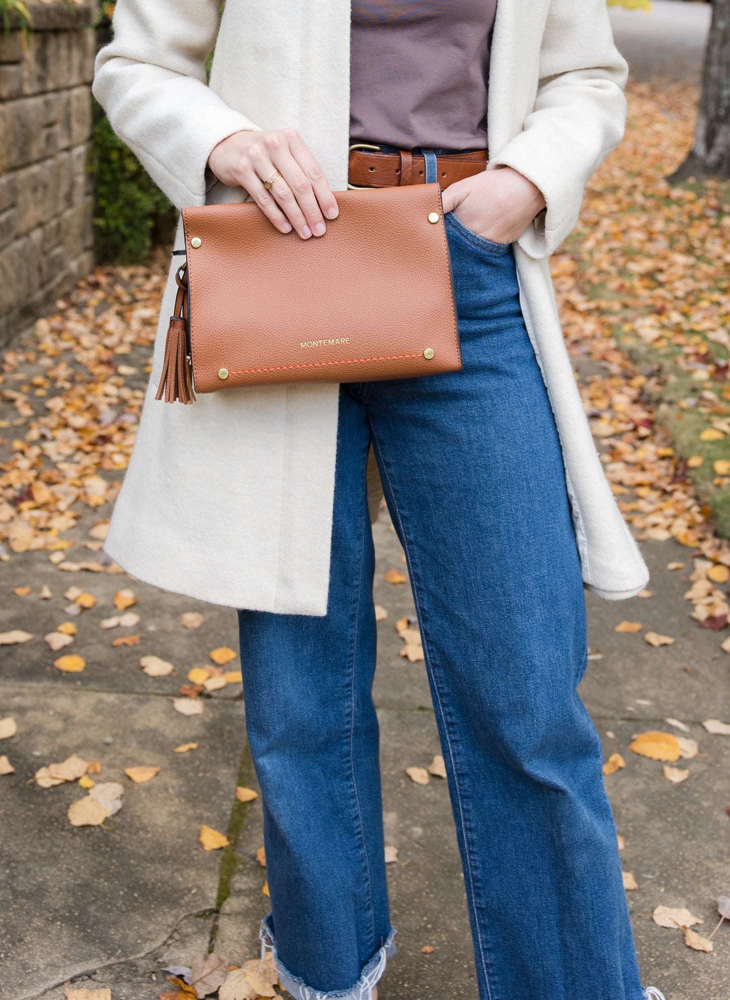Person holding a brown clutch bag outdoors on a leafy ground