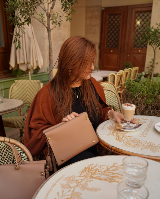 Woman sitting at a table with a beige handbag on her lap, surrounded by decorative elements.