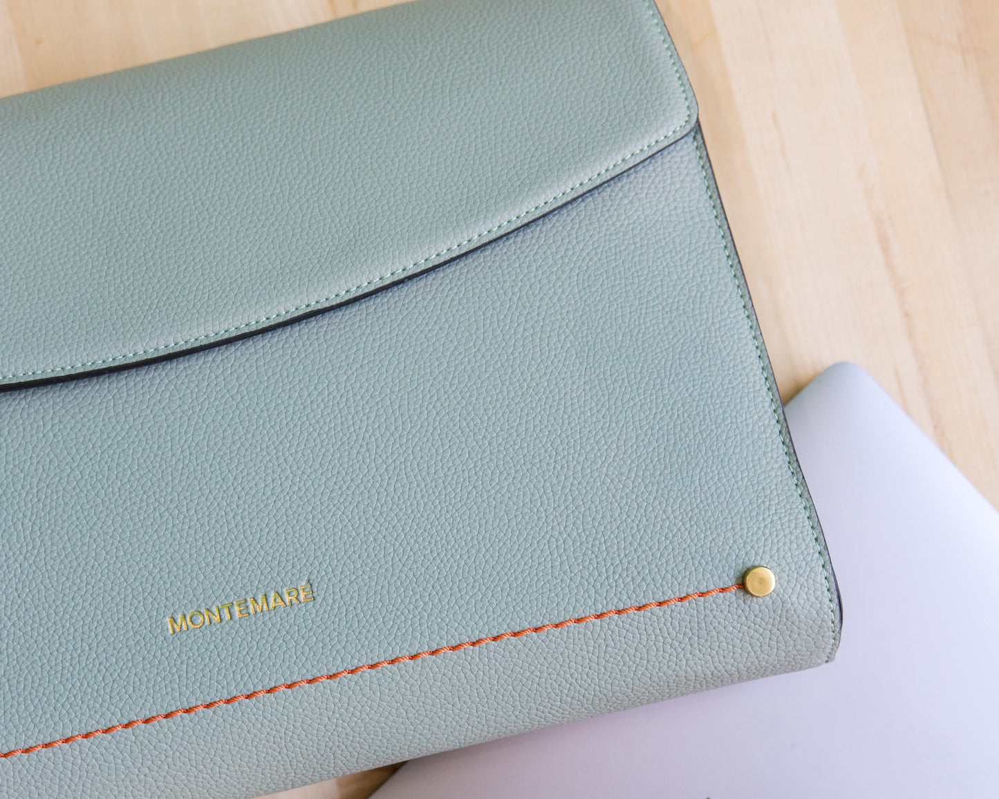 Light blue laptop sleeve with orange stitching on a light wood surface