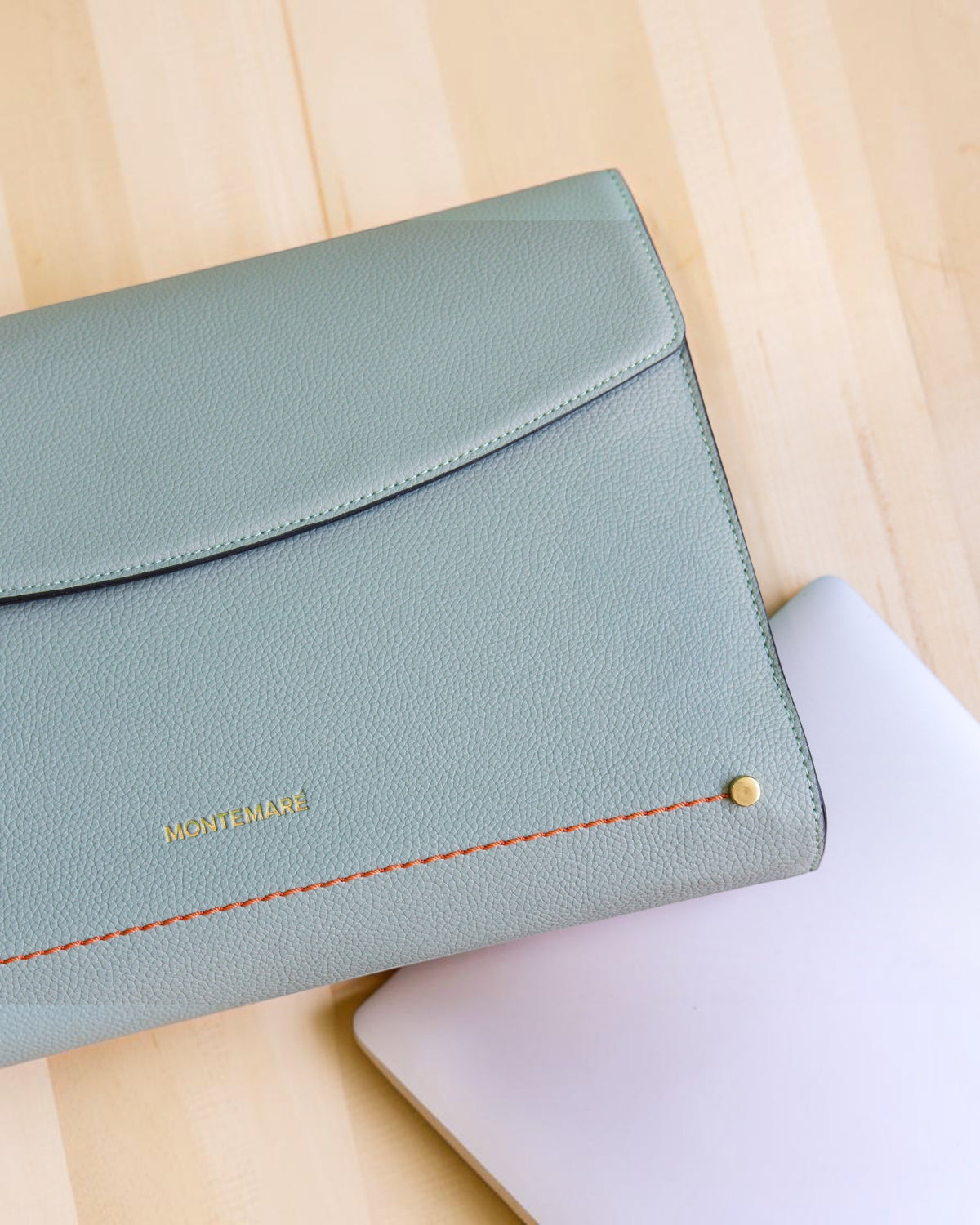 Light blue laptop sleeve with orange stitching on a light wood surface